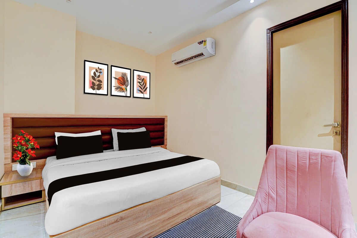 Quarto de hotel com cama, cadeira, mesa de cabeceira, planta em vaso e obras de arte na parede.