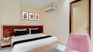 A hotel room with a bed, a chair, a nightstand, a potted plant, and wall art.