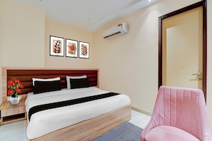 Quarto de hotel com cama, cadeira, mesa de cabeceira, planta em vaso e obras de arte na parede.