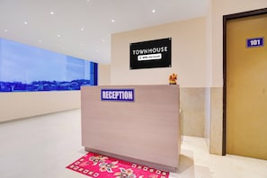 Un mostrador de recepción con un letrero que indica 'Townhouse' y 'Oyo-Serviced' en un vestíbulo moderno con vistas a un paisaje urbano.