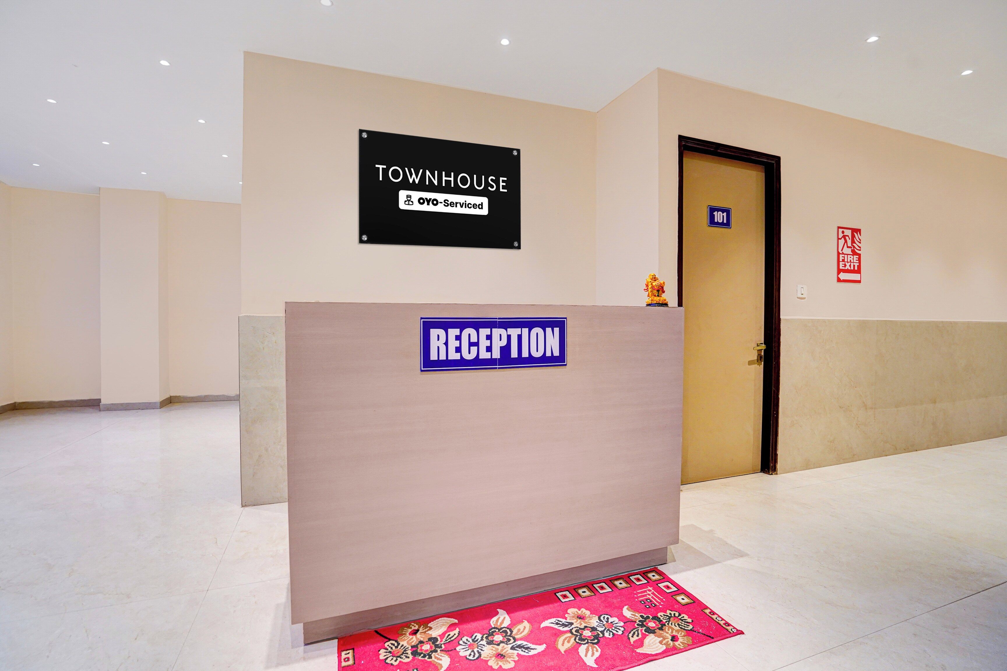 A reception desk with a sign indicating it's a townhouse serviced by OYO. There's a fire exit sign on the wall and a door marked with the number 101.
