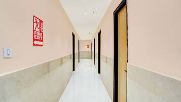 A corridor with a fire exit sign, doors, and a light switch on the wall.