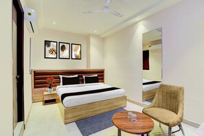 Habitación de hotel con cama, mesita de noche, silla, mesa redonda y una obra de arte en la pared.