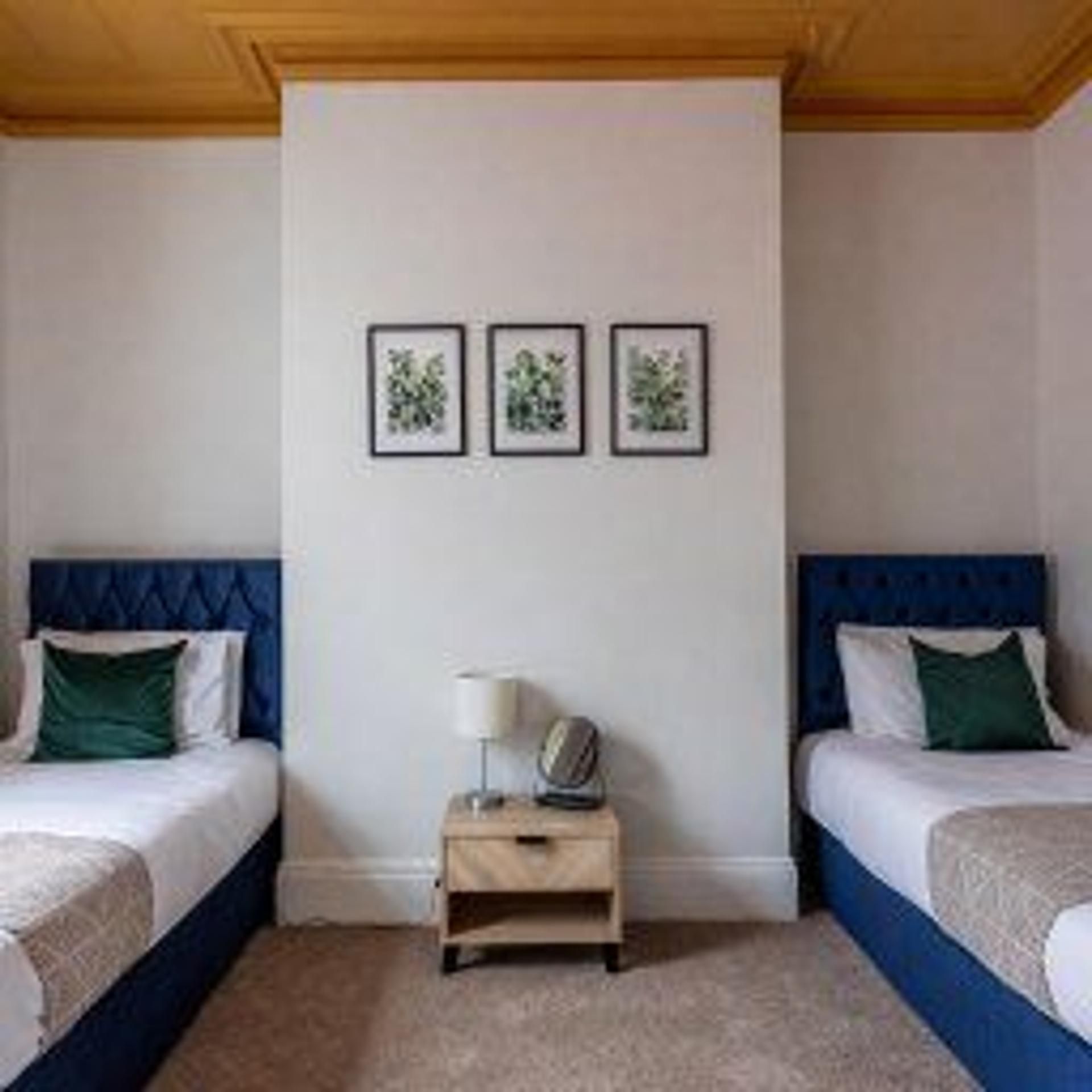 Une chambre d’hôtel avec deux lits, une table de chevet et trois tableaux encadrés accrochés au mur.