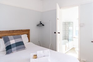 A bedroom with a wooden headboard, a checkered pillow, a white bedspread, a white towel, and two bottles on the bed. - Swift Host | Albany House | Sleeps 4 | Parking | Garden | Good Location (Norwich)