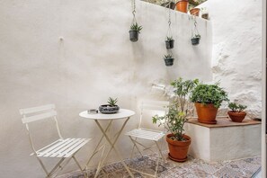 A small outdoor seating area with a white metal table and chairs, surrounded by potted plants and a white wall. - Authentic Porto Retreat with Private Patio (Porto)