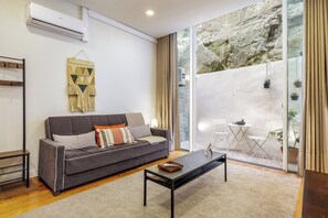 A modern living room with a grey sofa, a coffee table, and a large sliding glass door leading to an outdoor area with plants. - Authentic Porto Retreat with Private Patio (Porto)