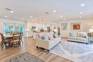 A spacious living area with a sofa, a dining table with chairs, a kitchen in the background, and a large rug. - Beautifully Decorated 4-bedroom house with Waterviews 7 minutes to Tyndall AFB (Panama City)