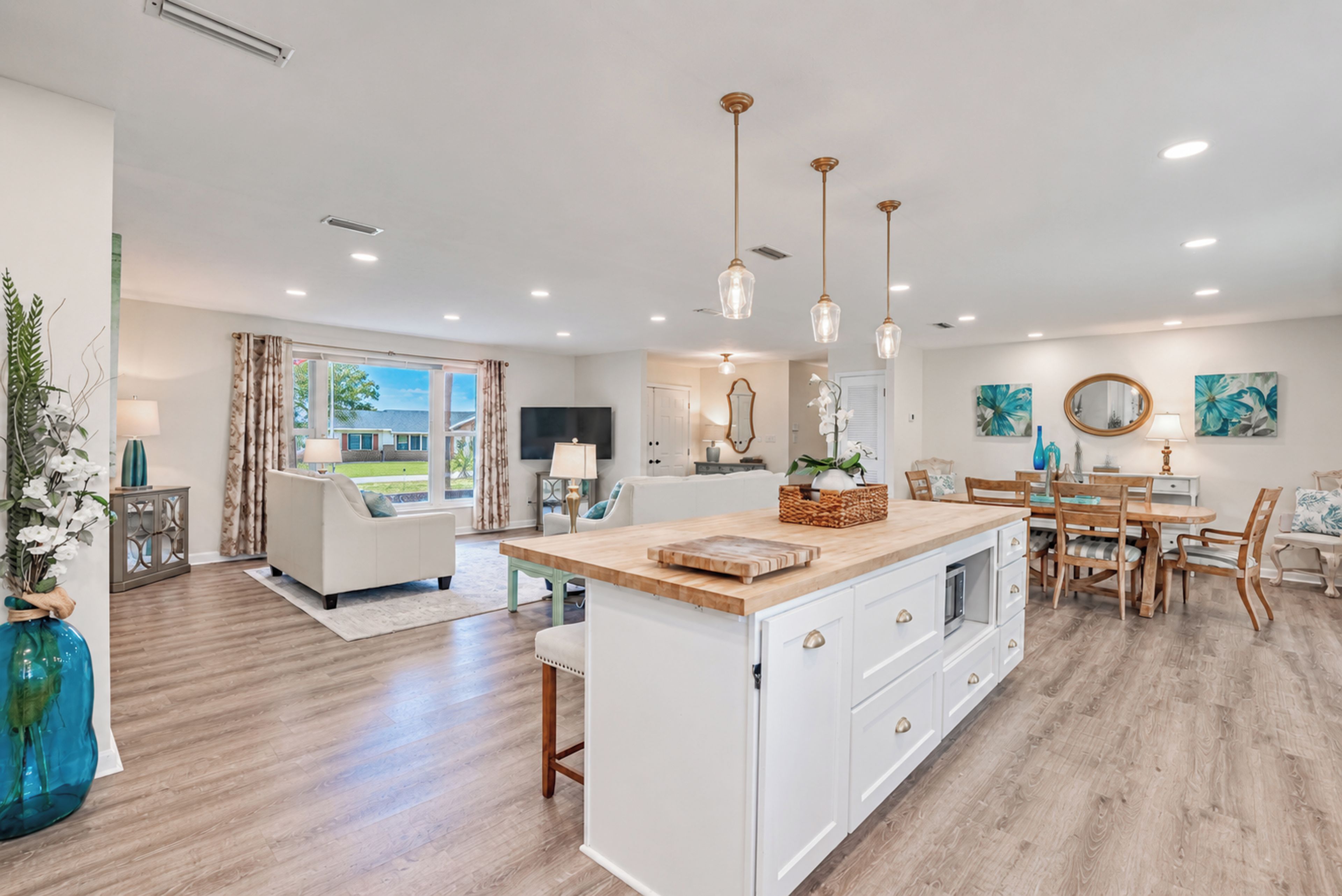 Cocina moderna con una isla central, comedor con sillas de madera y sala de estar con sofá y televisor.