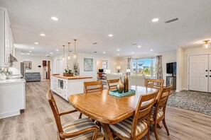 A spacious dining area with a wooden table and chairs, a kitchen in the background, and a view of the outdoors. - Beautifully Decorated 4-bedroom house with Waterviews 7 minutes to Tyndall AFB (Panama City)