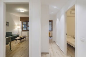 A modern interior with a living area featuring a sofa, a coffee table, and a lamp. There is a hallway leading to a bedroom with a bed. - XXV Aprile By Wonderful Italy - Menta (Genoa)