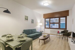 Een moderne woonkamer met een eethoek, een groene bank, een houten salontafel en een raam met zonwering.