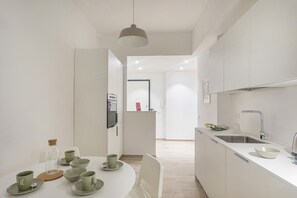 A modern kitchen with white cabinetry, a round dining table with matching chairs, and a pendant light. - XXV Aprile By Wonderful Italy - Menta (Genoa)