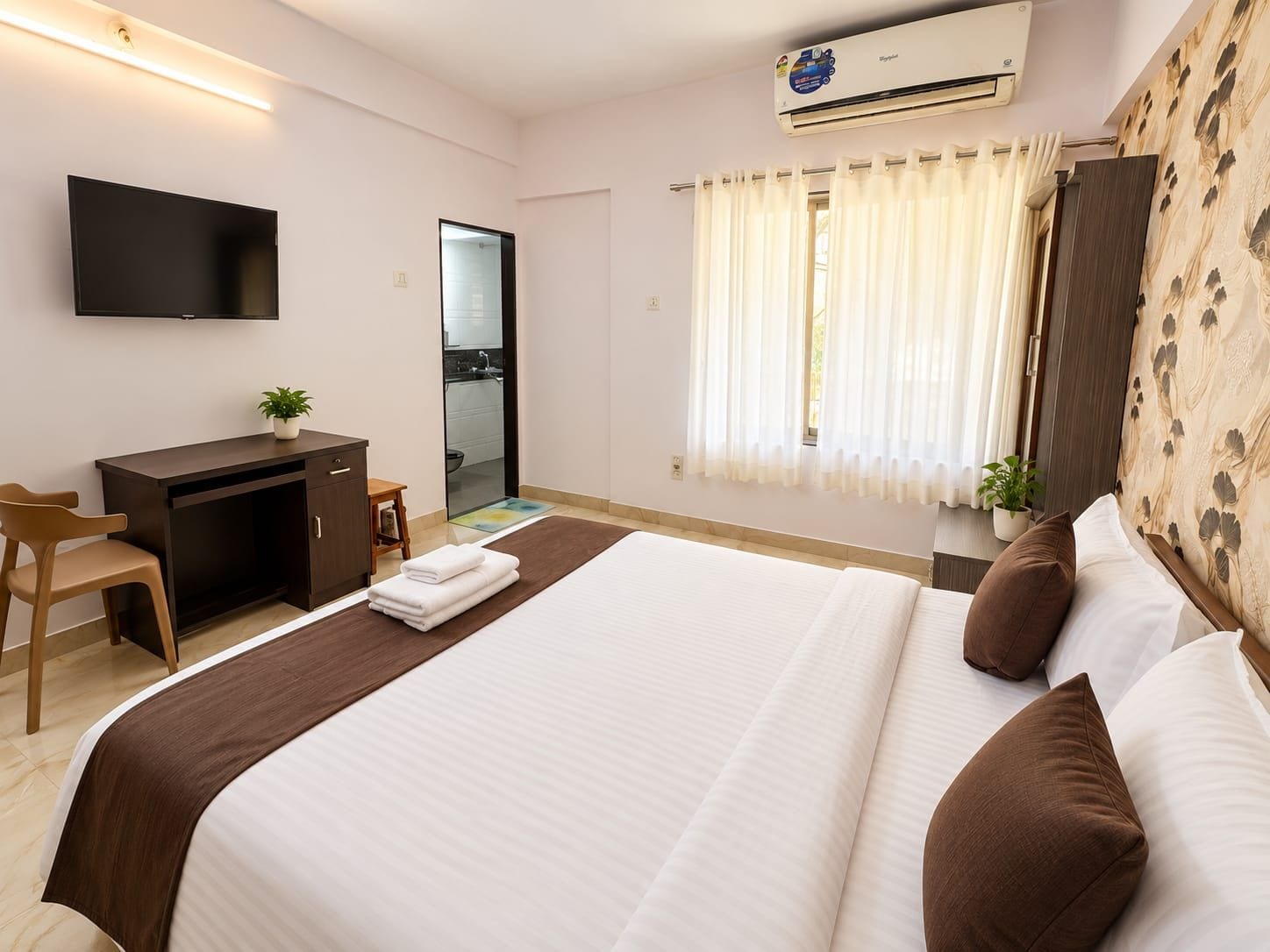 Habitación de hotel con cama, escritorio, silla, televisor, aire acondicionado y ventana con cortinas.