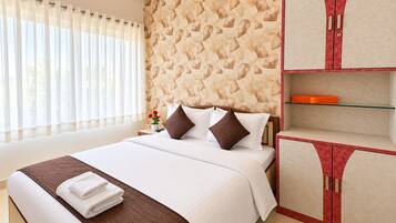 Una habitación de hotel con cama, mesita de noche, pared con diseño de hojas, ventana con cortinas y armario con detalle rojo.
