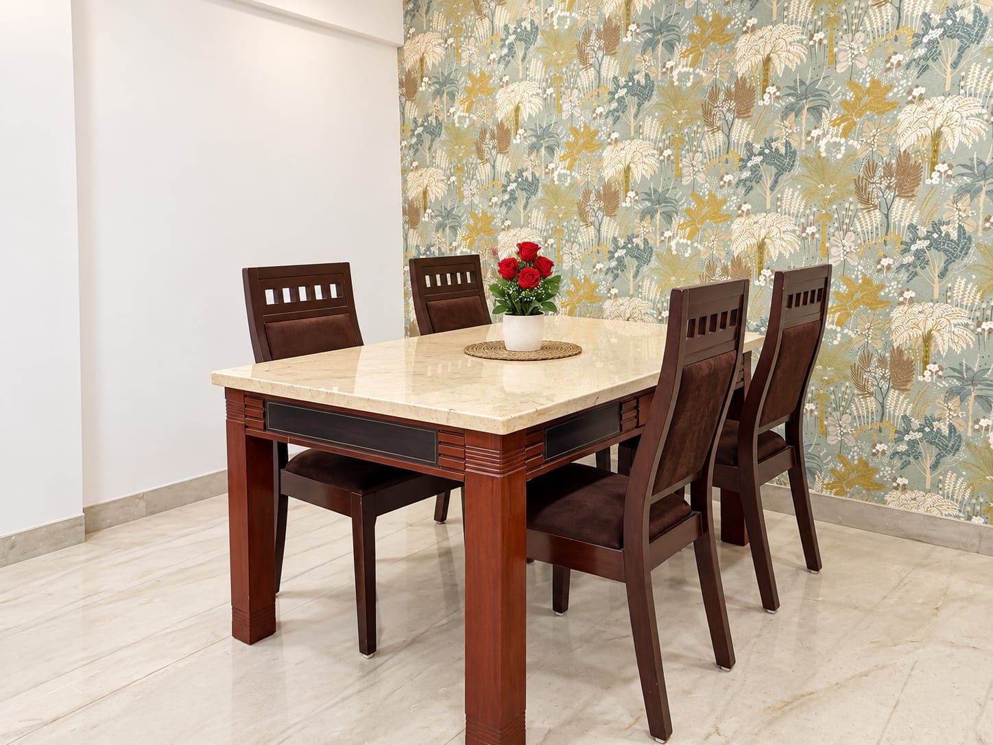 A dining table with six chairs, a vase with red flowers, and a floral wallpaper.