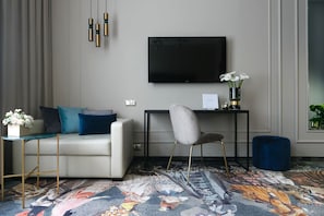 En moderne stue med en sofa, en lænestol, et fladskærms-tv, et lille bord med en blomsterbuket og et mønstret tæppe.