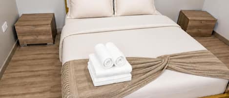 A neatly made bed with a headboard, two bedside tables, and a folded towel on the bed.