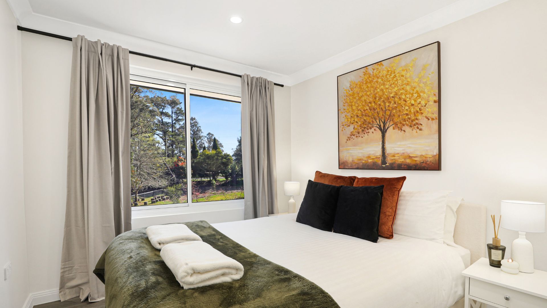 Une chambre d’hôtel avec un lit, un tableau représentant un arbre et une vue sur l’extérieur.