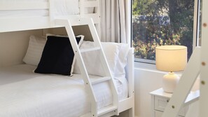 Un lit superposé avec une échelle, une table de chevet avec une lampe et une fenêtre donnant sur un paysage verdoyant.
