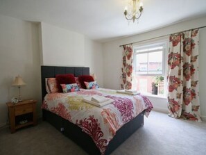 A bedroom with a bed, a nightstand, a window with curtains, and a chandelier. - Three bedroom  in United Kingdom of Great Britain and Northern Ireland, Norwich (Norwich)