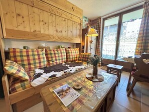 A cozy room with a sofa, a table with a magazine, a lamp, and a view of the outside. - Ground floor, tv, ski locker, 24m², Praz sur Arly (Praz-sur-Arly)