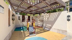 A playground with a slide and climbing structures, surrounded by walls and a pergola. - Burj Khalifa View 2BR in the Heart of Downtown, Short Walk from Wings of Mexico (Dubai)