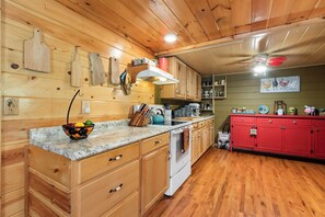 A kitchen with wooden cabinets, a red cabinet, a stove, and a sink. - Cozy 3BR Mountain Cabin | Peaceful & Relaxing (Murphy)