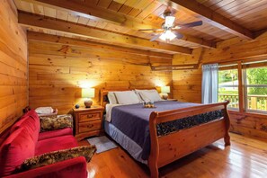Een slaapkamer in een houten hutje, met een bed, nachtkastjes, een rode bank en een raam met gordijnen.