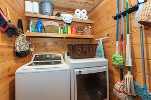 Een wasserette met een wasmachine, planken met schoonmaakmiddelen en verschillende schoonmaakspullen.