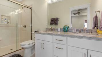 A modern bathroom with a glass shower enclosure, a white toilet, a vanity with a marble countertop, and a ceiling fan.