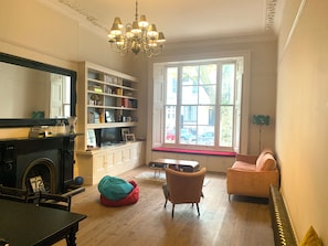 Ein Wohnzimmer mit Kamin, Bücherregalen, einer Couch und einem Fenster mit Blick auf die Straße.