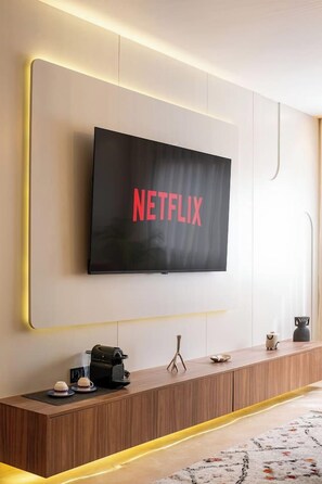 Ein modernes Wohnzimmer mit einem an der Wand befestigten Flachbildfernseher, der 'NETFLIX' in roten Buchstaben anzeigt.