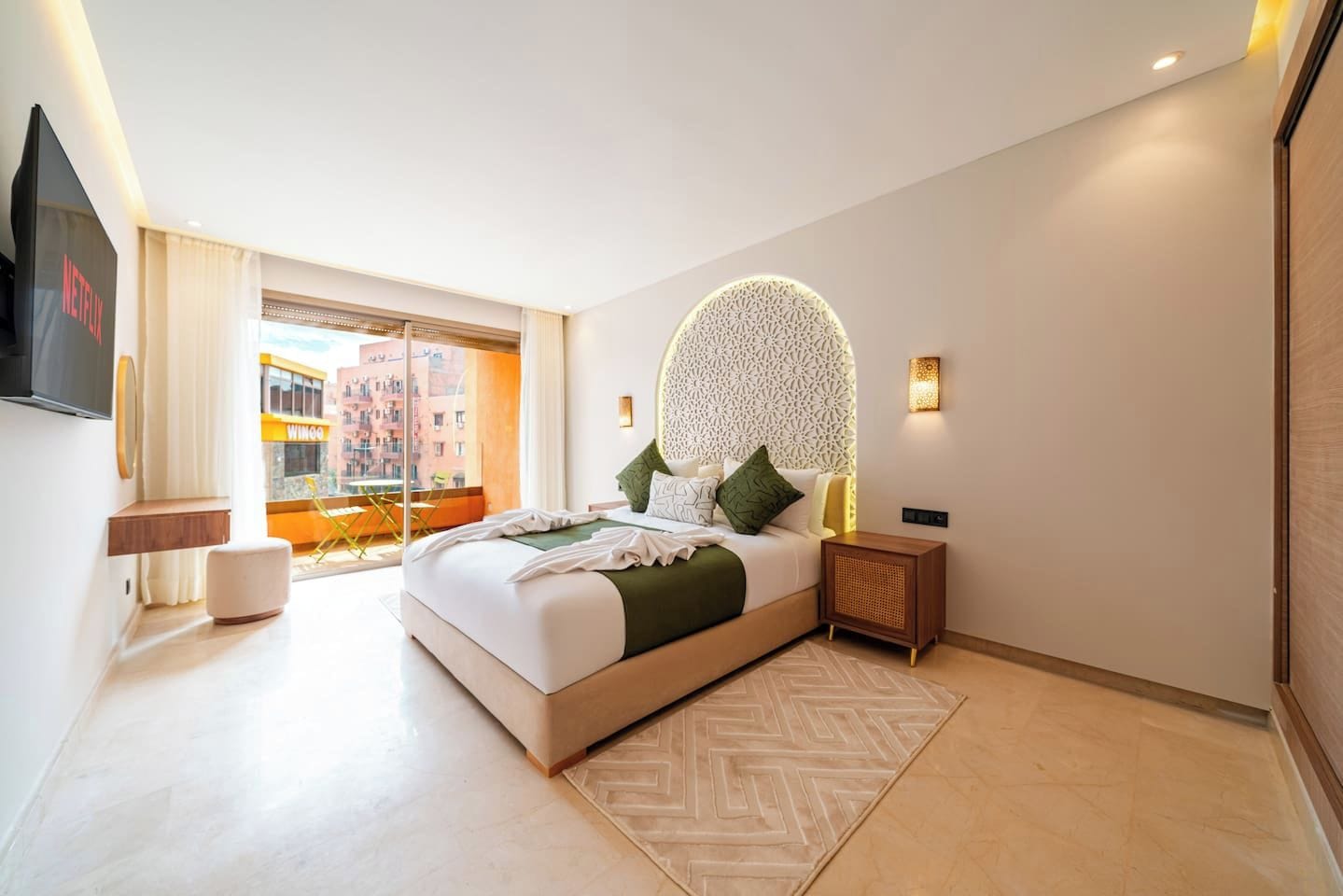 Ein modernes Hotelzimmer mit einem großen Bett, einem Fernseher, einer dekorativen Wandleuchte und Blick auf die Stadt.