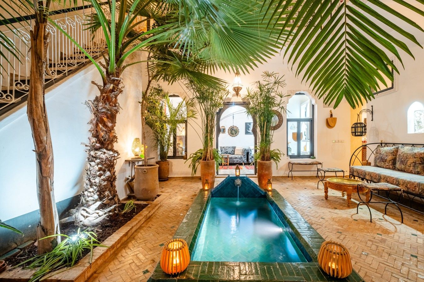 Zona de piscina con una fuente, rodeada de plantas en macetas y un área de descanso con sofá y sillones.