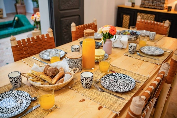 A breakfast table set with plates, glasses, and a basket of bread. - Riad Des Sables • Pool • 15 min walk Jemaa El Fna (Marrakesh)