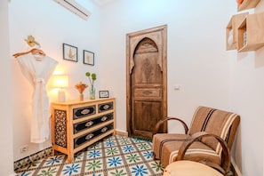 A room with a wooden cabinet, a patterned floor, a door with intricate carvings, and a chair with a striped cushion. - Riad Des Sables • Pool • 15 min walk Jemaa El Fna (Marrakesh)