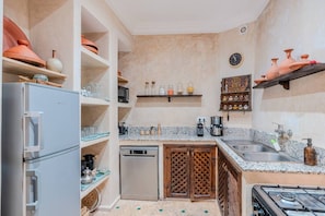 A compact kitchen with a refrigerator, dishwasher, stove, and shelves with kitchenware. - Riad Des Sables • Pool • 15 min walk Jemaa El Fna (Marrakesh)