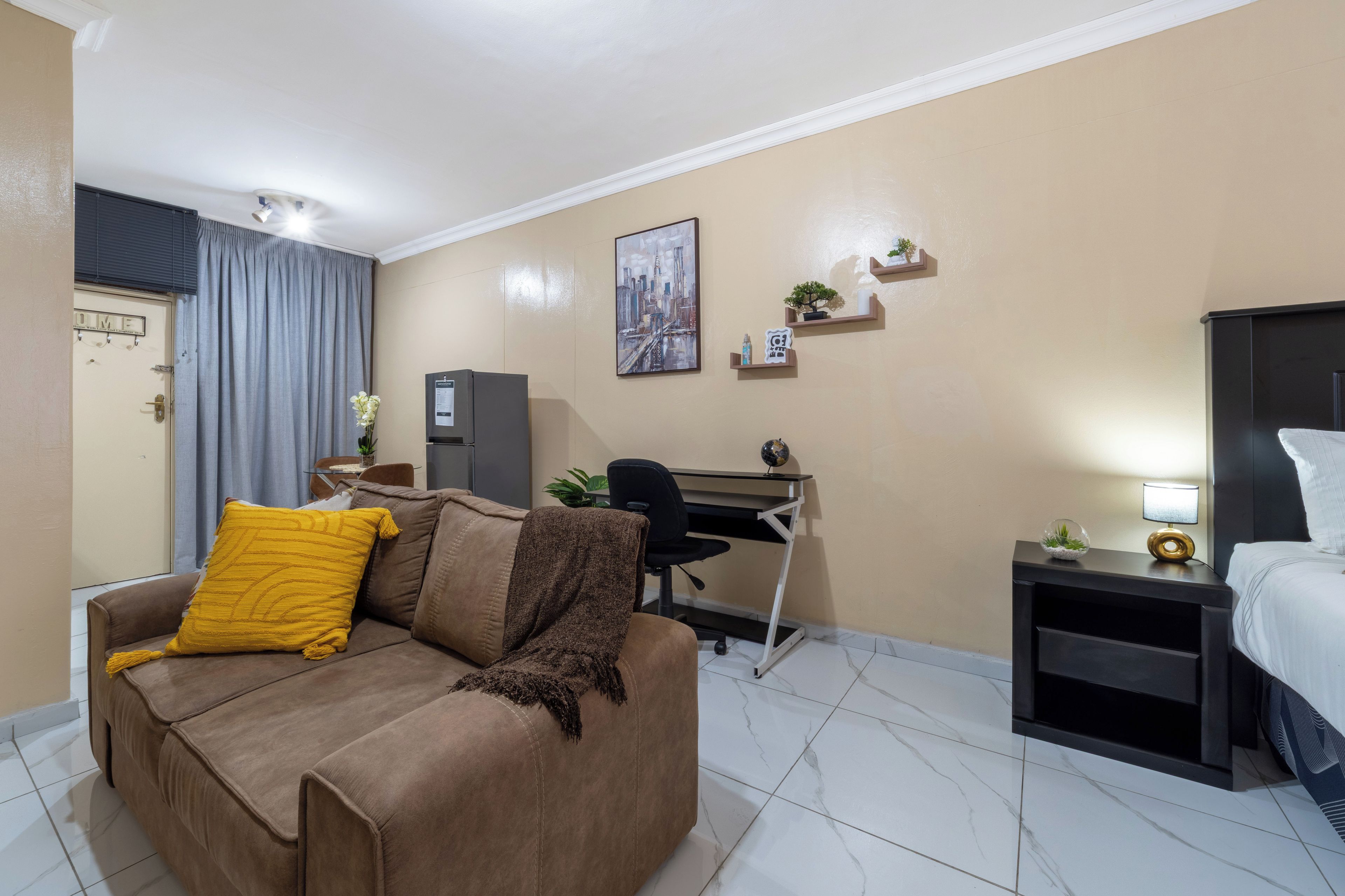Quarto de hotel com sofá, escrivaninha, cama e mesa de cabeceira com abajur.