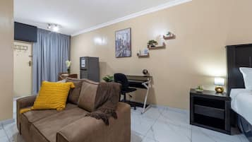 Quarto de hotel com sofá, escrivaninha, cama e mesa de cabeceira com abajur.