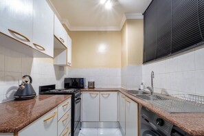 A compact kitchen with white cabinets, a microwave, a kettle, and a dishwasher.