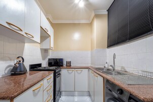 A compact kitchen with white cabinets, a microwave, a kettle, and a dishwasher.
