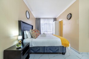 A hotel room with a bed, a nightstand, a lamp, a window with curtains, and a door.