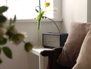 A room with a white table, a Marshall amplifier, a vase with flowers, and a window. - Teestuuv - Cozy 60 square meters for 2 people in the heart of Husum (Husum)
