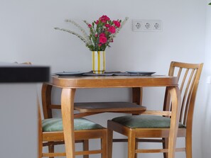 A wooden dining table with a vase of flowers, two chairs with green cushions, and a power outlet on the wall. - Teestuuv - Cozy 60 square meters for 2 people in the heart of Husum (Husum)
