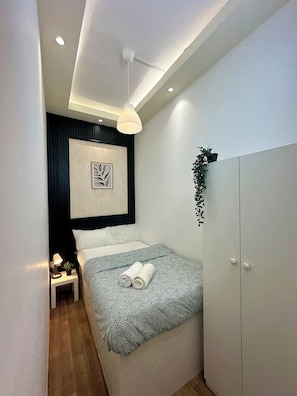 Een moderne slaapkamer met een bed, nachtkastje, lamp en een aan de muur bevestigde plant.