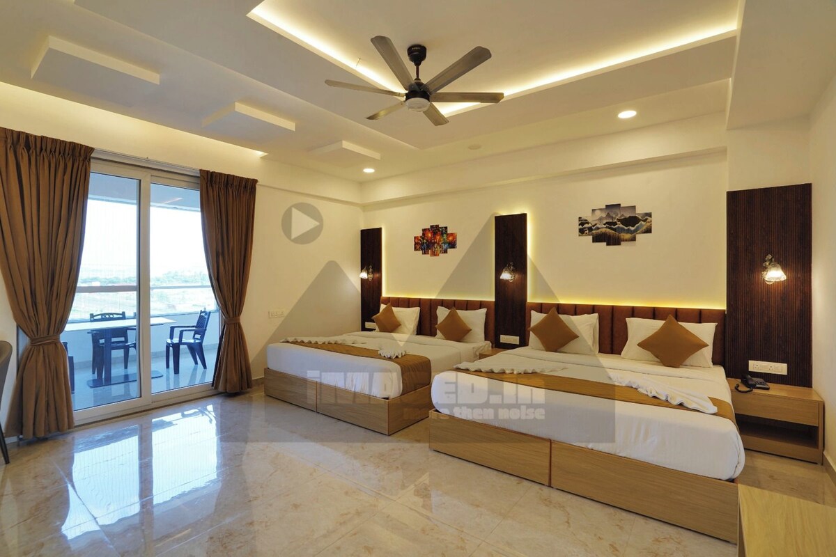 A hotel room with two beds, a ceiling fan, a large window with curtains, and a view of the outdoors.