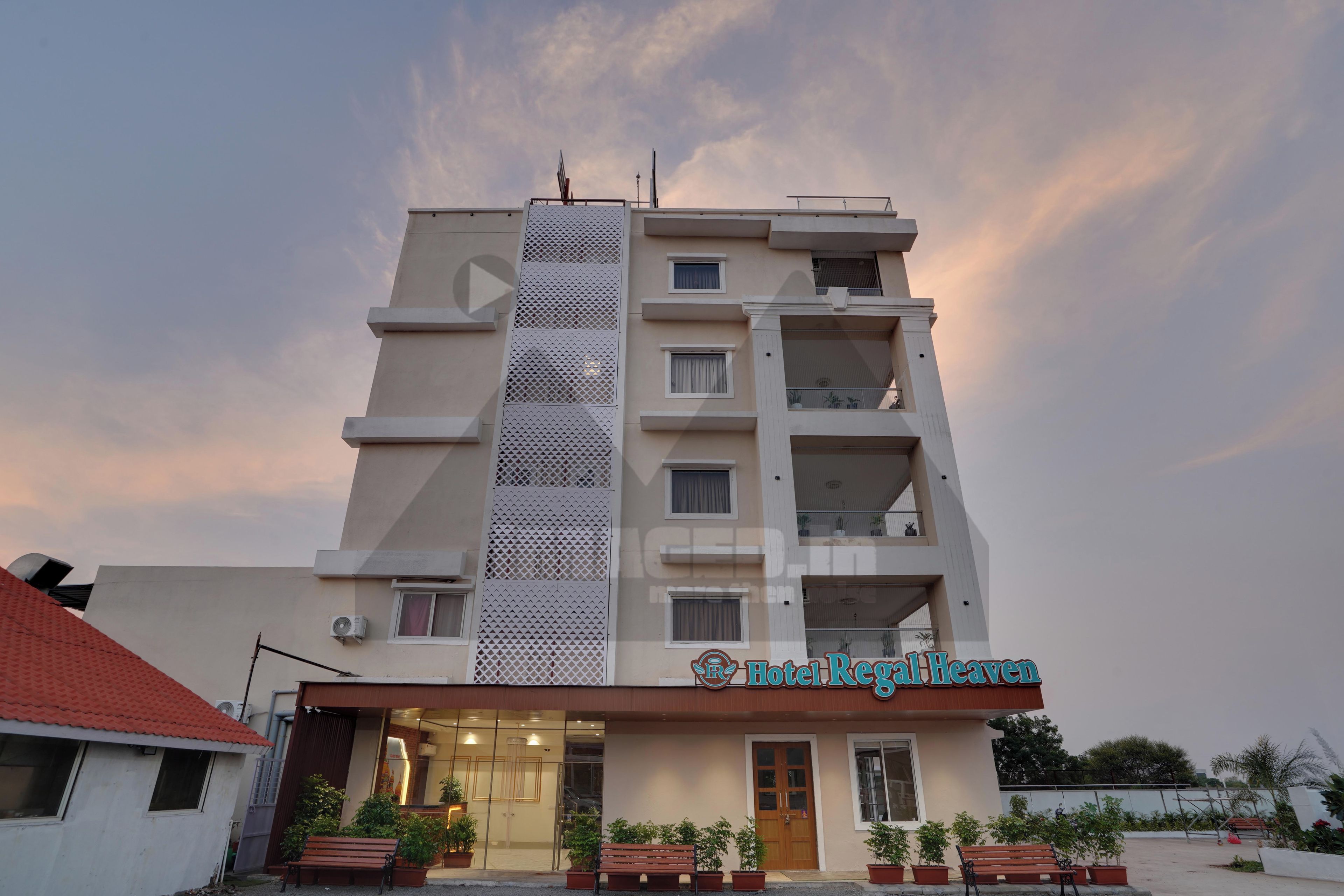 A multi-story hotel with a modern facade, a prominent entrance, and a balcony with potted plants.