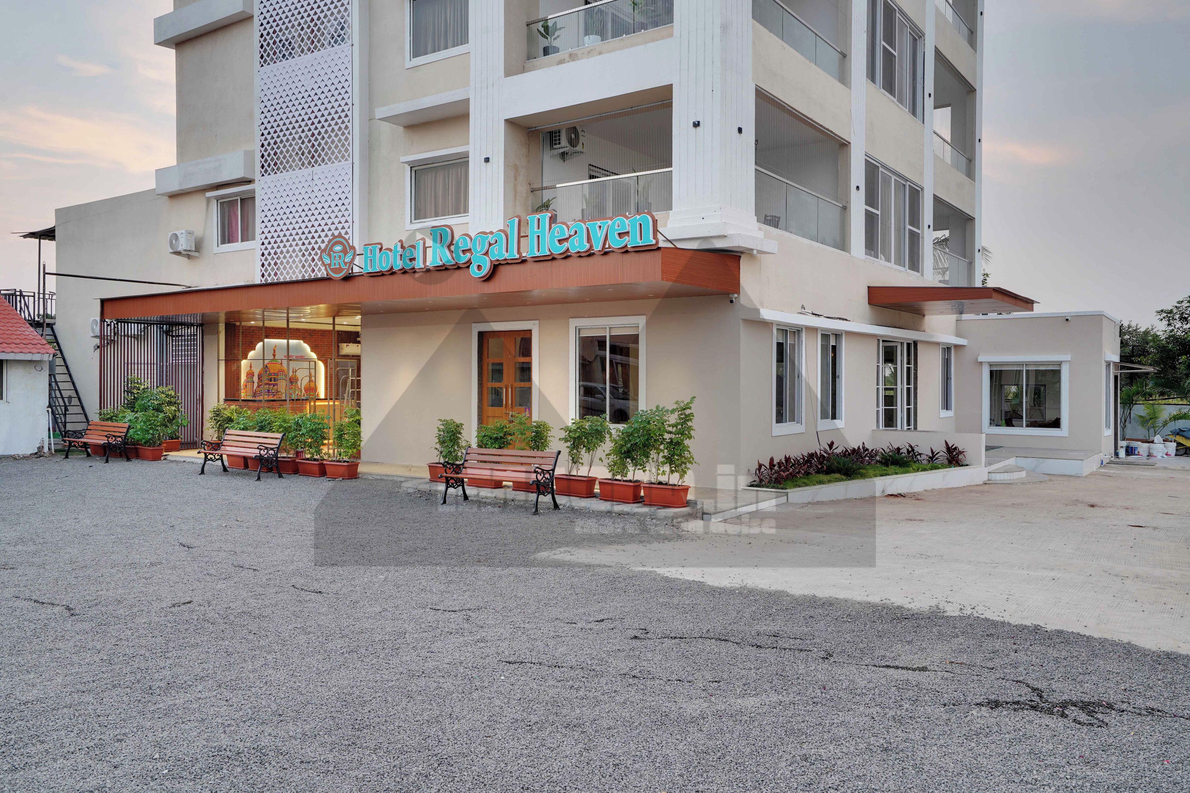 Hotel amb un rètol que diu 'Hotel Regal Heaven', amb una façana moderna, balcons, una entrada tancada amb reixa i seients a l'aire lliure.