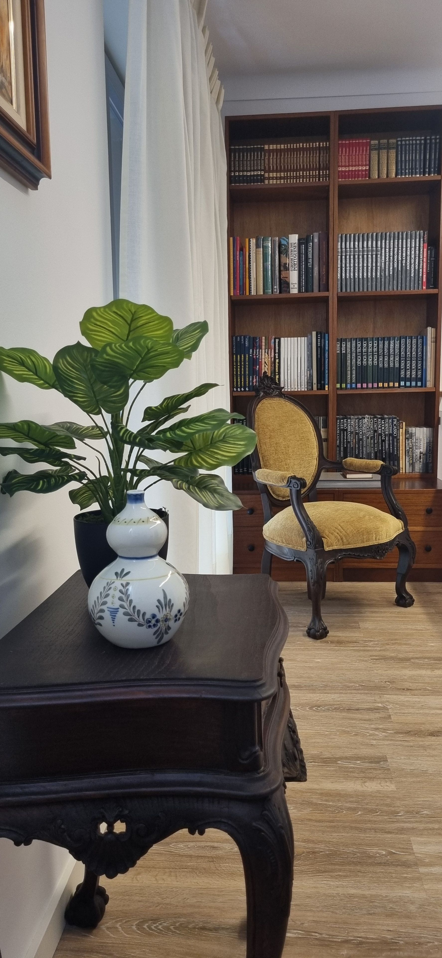 A room with a dark wooden table, a chair, a potted plant, and a bookshelf filled with books.